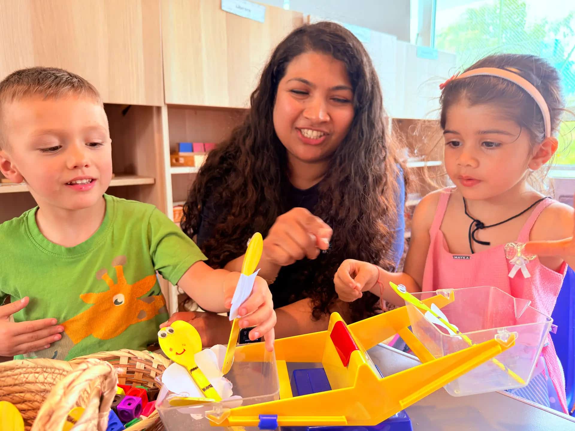 An educator engaging two young children in a hands-on Montessori activity at Blue Nest Montessori Pinner