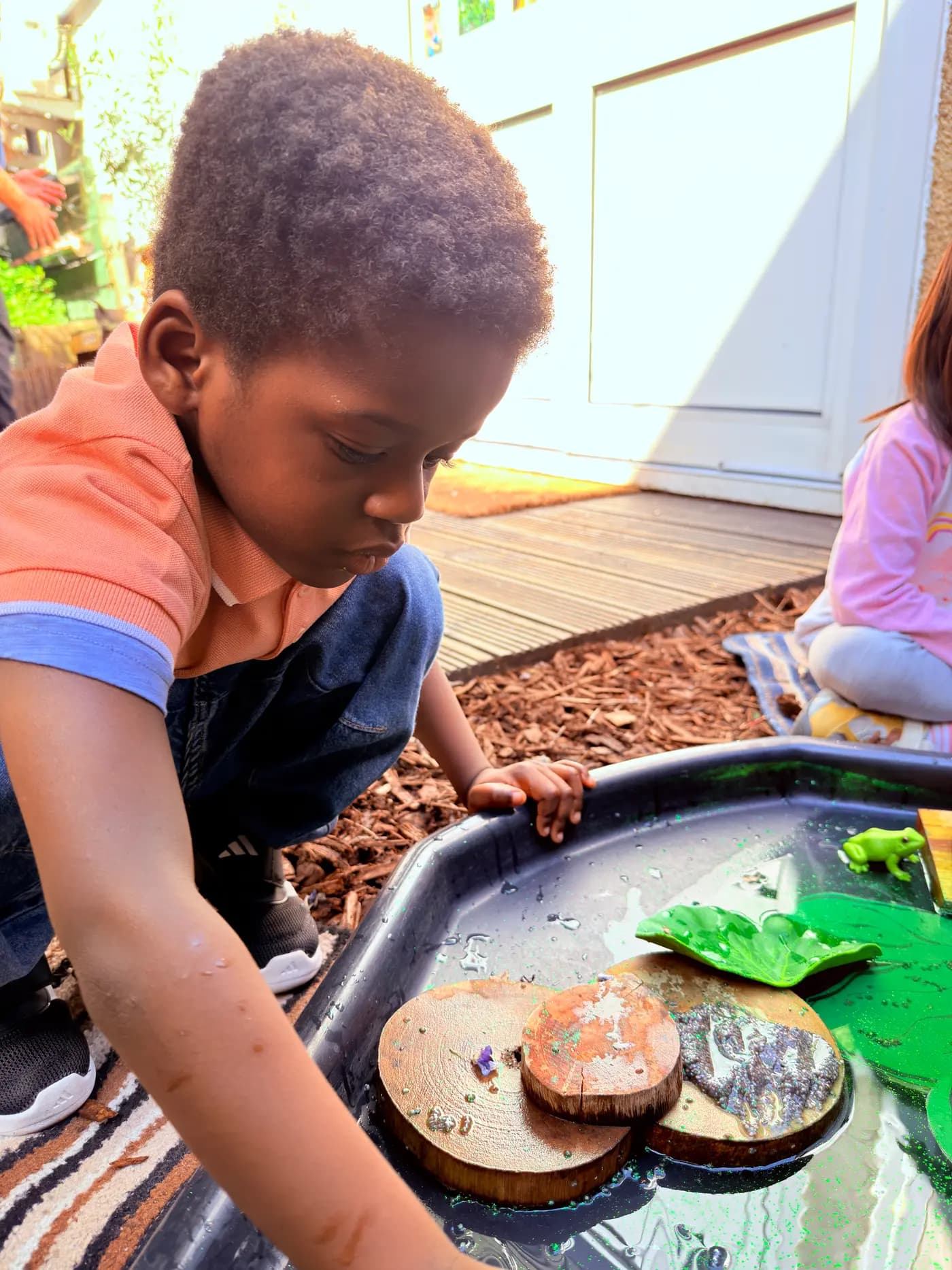 Child investigating natural materials in an outdoor tray at Blue Nest Montessori Harrow