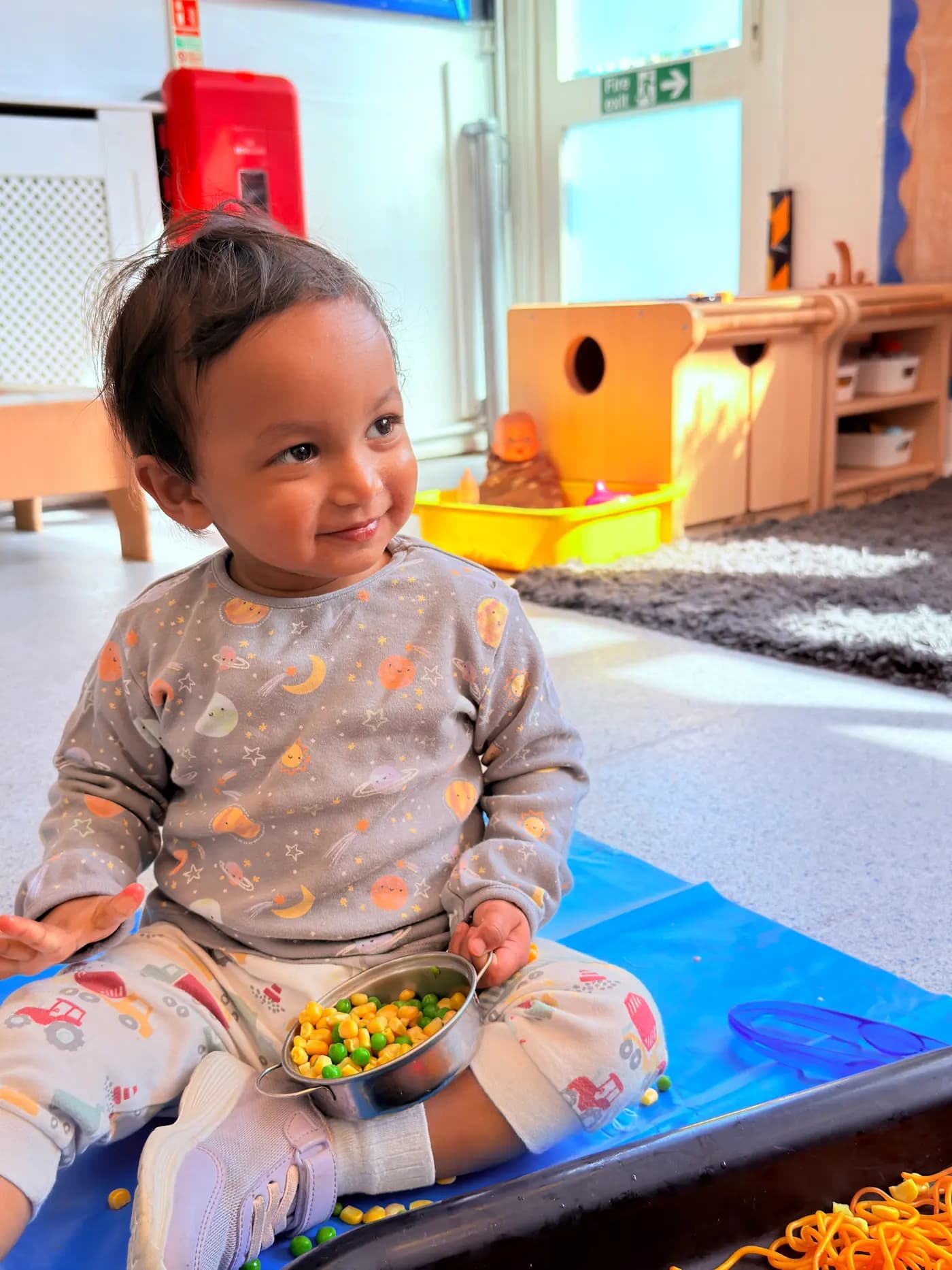 Toddler exploring a bowl of sweetcorn and peas at Blue Nest Montessori Harrow