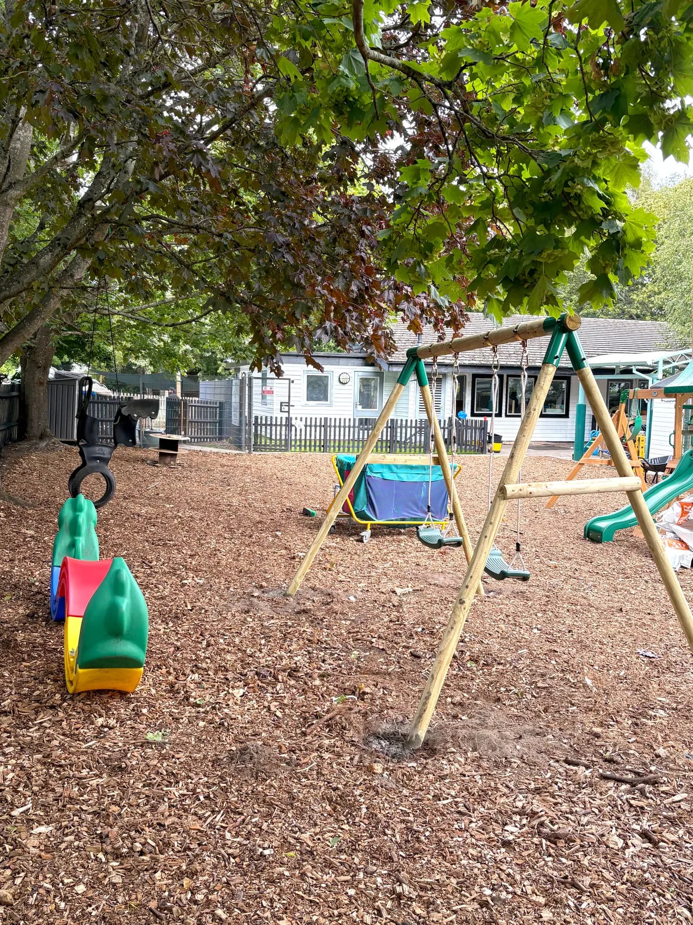 The outdoor playground at Blue Nest Montessori Aldershot with swings under mature trees